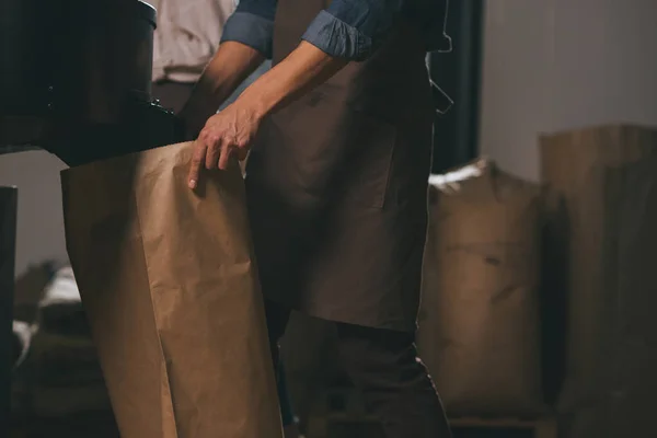 Partial view of worker in apron with paper bags of coffee beans — Stock Photo