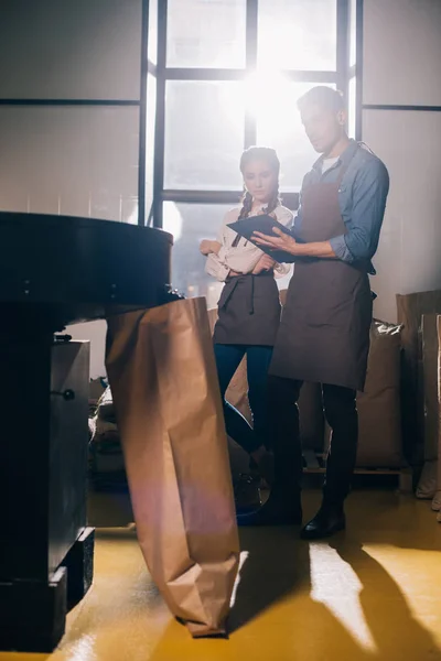 Young coffee roasters checking coffee beans roasting process together in coffee shop — Stock Photo