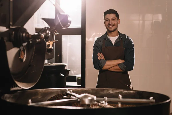 Portrait de torréfacteur de café souriant debout à la machine de torréfaction et regardant la caméra — Photo de stock