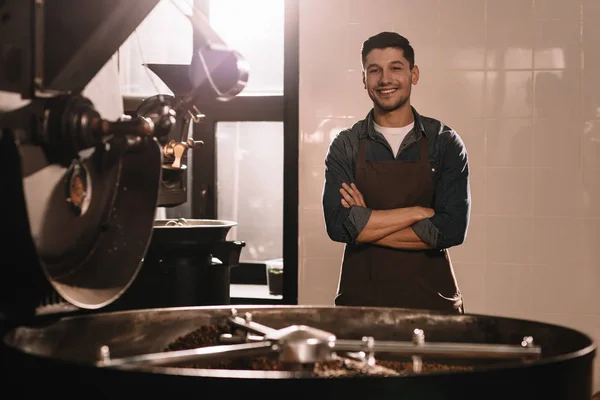 Retrato de sorrindo torrador de café em pé na máquina de torrefação e olhando para a câmera — Fotografia de Stock