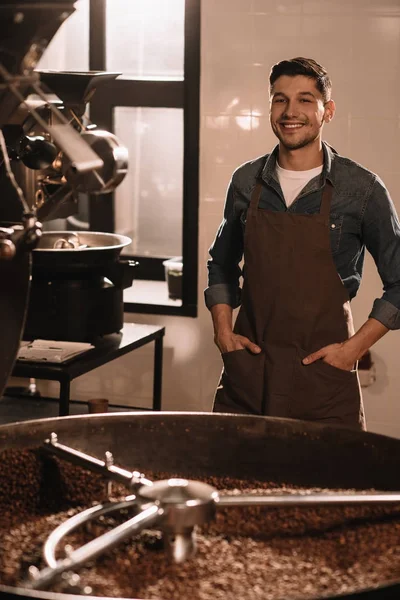 Ritratto di torrefazione sorridente del caffè che si leva in piedi alla macchina torrefazione e che guarda la macchina fotografica — Foto stock