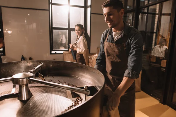 Coffee roaster roasting coffee beans in roasting machine with colleague near by — Stock Photo