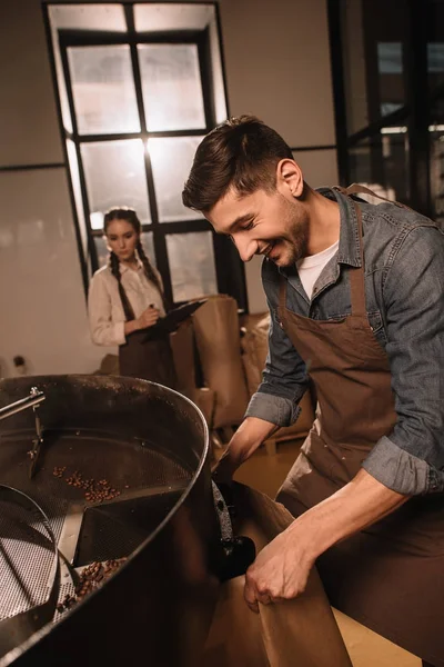 Кофе жаровня обжига кофейных зерен в жаровне машина с коллегой рядом — стоковое фото