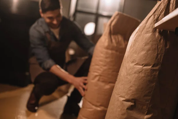 Vista parcial del trabajador en delantal con bolsas de papel de granos de café - foto de stock