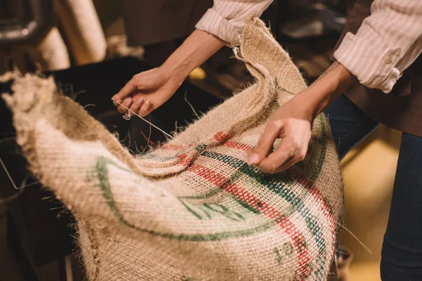 Partial view of worker tying sack bag with coffee beans — Stock Photo