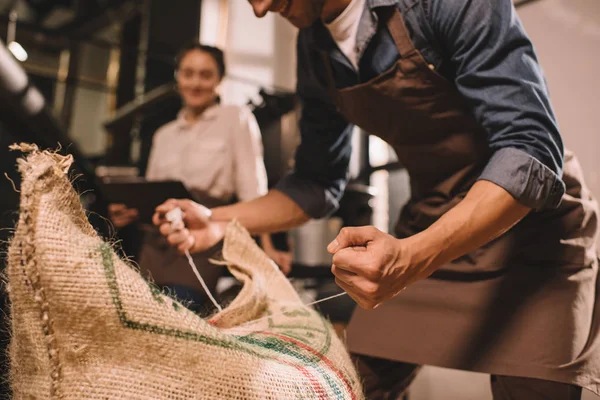 Vista parcial del trabajador atando saco bolsa con granos de café - foto de stock