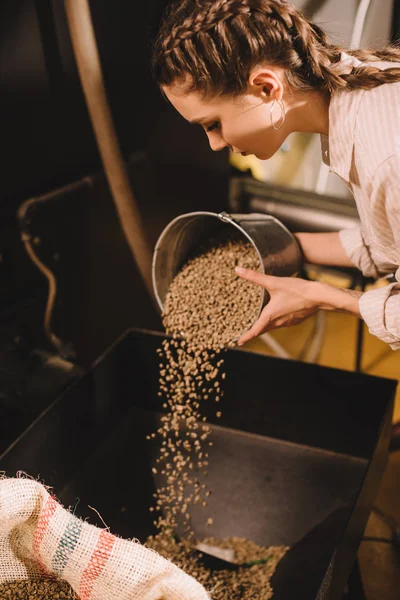 Vue latérale du jeune travailleur versant des grains de café dans le récipient — Photo de stock