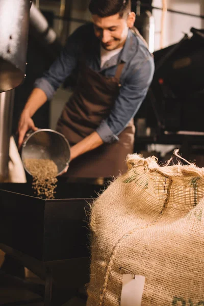 Selective focus of coffee roaster pouring coffee beans into roasting machine — Stock Photo