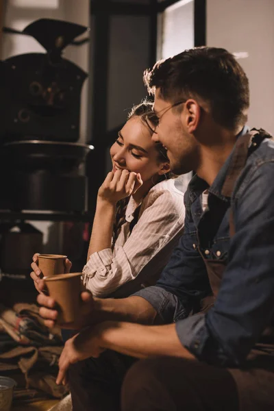 Sonriente pareja con tazas de café teniendo descanso durante el trabajo en la cafetería - foto de stock