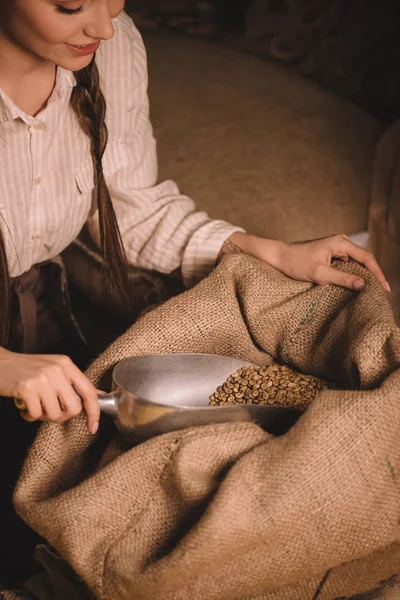 Partial view of worker gathering coffee beans with metal scoop from sack bag — Stock Photo