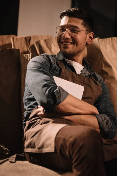 Sonriente joven trabajador con tableta sentado en saco - foto de stock
