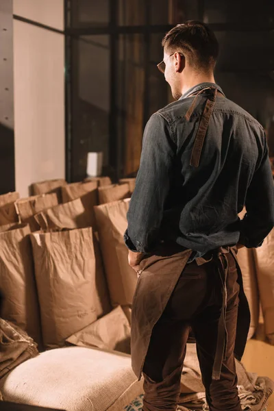 Vue arrière du travailleur de café dans le tablier regardant les sacs en papier avec des grains de café — Photo de stock