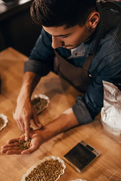 Foco seletivo do homem verificando a qualidade dos grãos de café na mesa de madeira — Fotografia de Stock