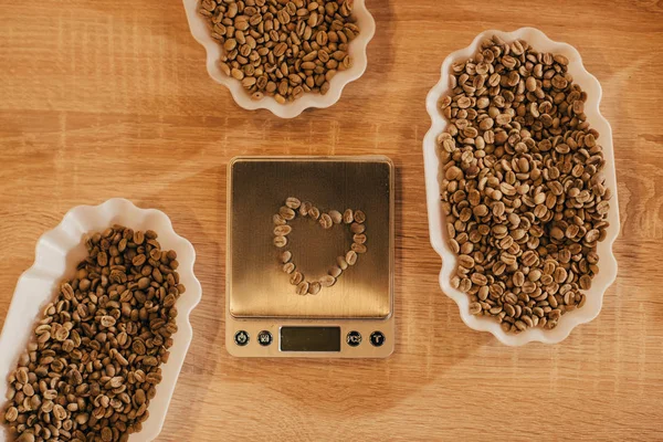 Vista dall'alto di disposizione di ciotole con chicchi di caffè per la funzione alimentare e bilance da cucina su tavolo in legno — Foto stock