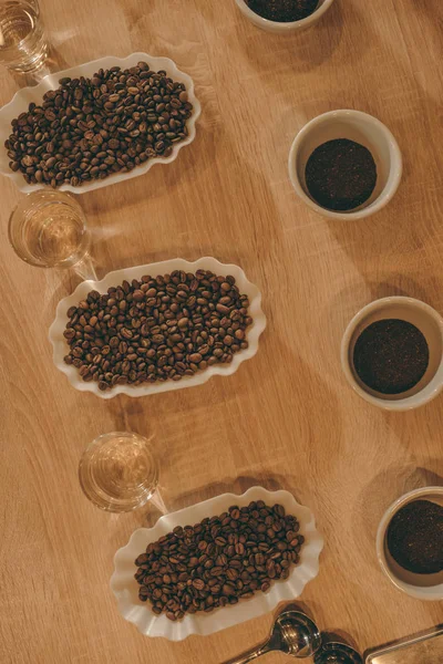 Draufsicht auf die Anordnung von Schalen mit Kaffeebohnen und Wassergläsern für die Nahrungsmittelfunktion auf einer hölzernen Tischplatte — Stockfoto