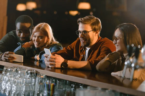 Compañía de jóvenes que utilizan teléfonos inteligentes en el bar - foto de stock