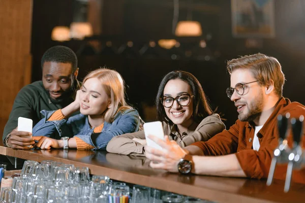 Молодая привлекательная компания в баре, глядя на экран смартфона — стоковое фото