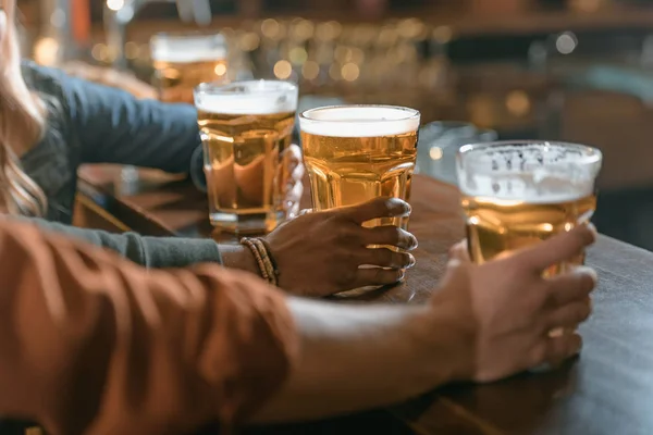 Imagen recortada de la empresa sosteniendo vasos con cerveza en el bar - foto de stock