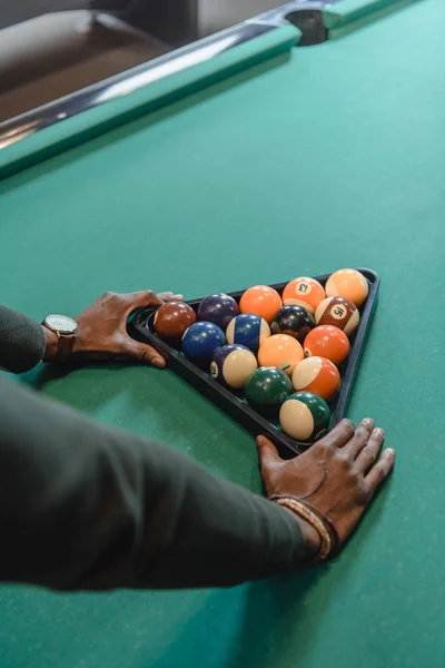 Imagen recortada de manos masculinas formando conjunto de bolas de billar por triángulo - foto de stock