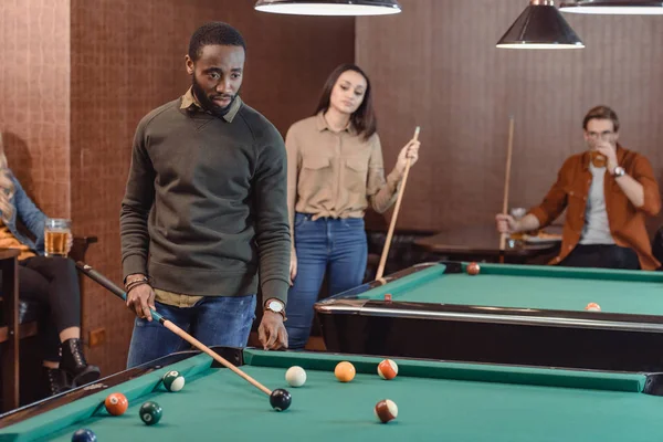 African american man playing in pool at bar with friends — Stock Photo