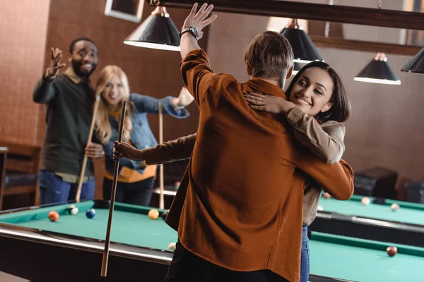 Rückansicht junger Freunde, die sich am Billardtisch an der Bar umarmen — Stockfoto