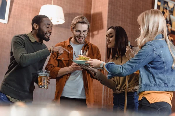 Amigos multiculturales en el bar con cerveza y comida - foto de stock