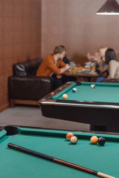 Company of multiethnic friends eating and drinking beside pool table at bar — Stock Photo