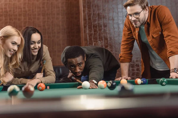 Young attractive multiethnic friends playing in pool at bar — Stock Photo