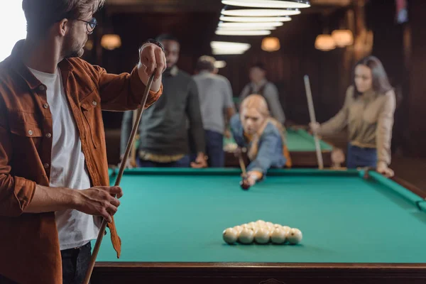 Jeune homme craie cue à côté de la table de billard au bar avec des amis — Photo de stock