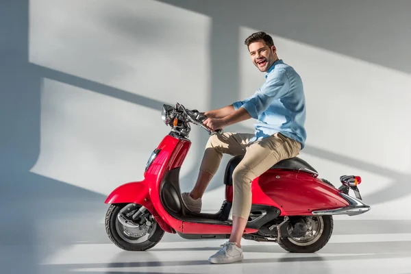 Vista laterale di giovane uomo allegro seduto su scooter rosso — Foto stock