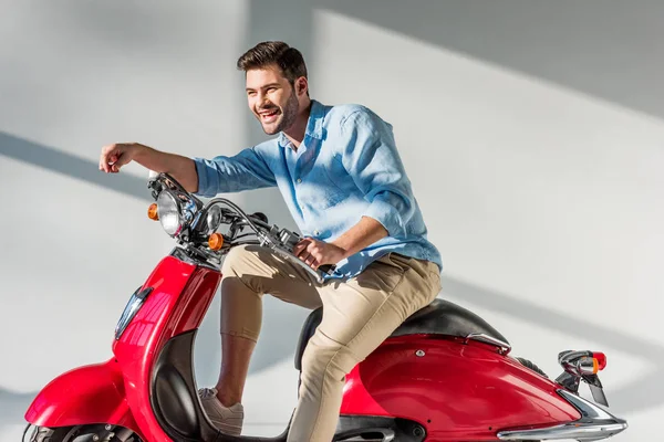 Vista lateral del joven hombre alegre sentado en scooter rojo - foto de stock