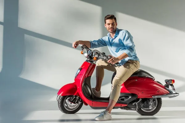 Side view of young man looking at camera while sitting on red scooter — Stock Photo