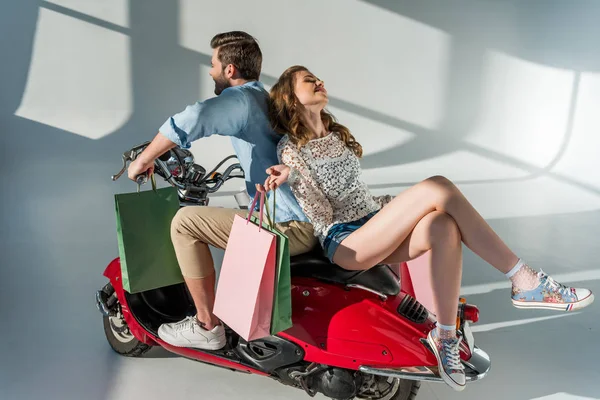 Stylish couple in love with shopping bags sitting on red scooter — Stock Photo
