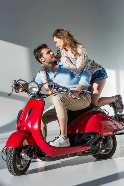 Вид сбоку стильной молодой пары на красном скутере, смотрящей друг на друга — стоковое фото