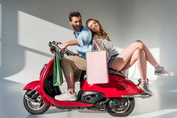 Stylish couple in love with shopping bags sitting on red scooter — Stock Photo