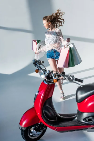 Feliz joven con bolsas de compras corriendo a scooter - foto de stock