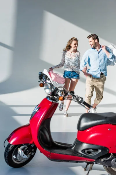 Feliz pareja con bolsas de compras caminando a scooter rojo - foto de stock