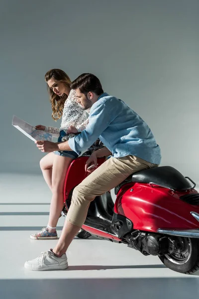 Young couple looking for destination on map in hands while sitting on red scooter — Stock Photo