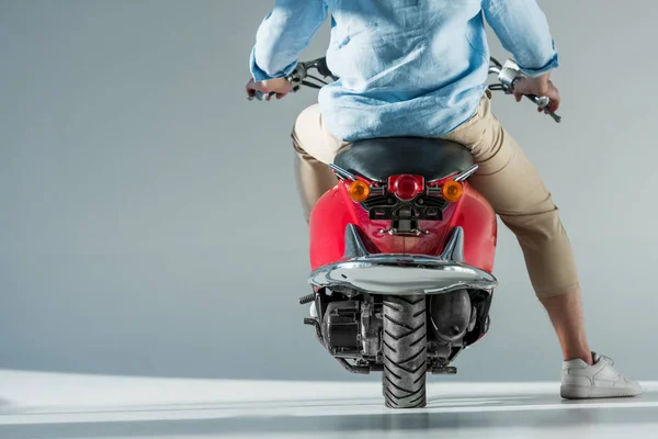 Частичный вид человека в стильной одежде, сидящего на красном скутере — стоковое фото