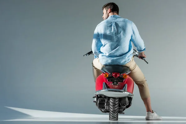 Вид сзади модного человека в рубашке, сидящего на красном скутере — стоковое фото