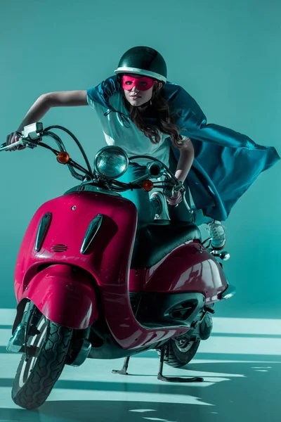 Donna in costume da supereroe e casco protettivo cavalcando scooter rosso — Foto stock