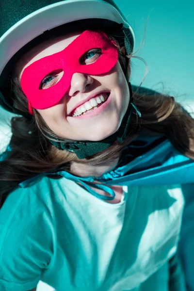 Ritratto di donna allegra in casco, maschera da supereroe e mantello guardando la macchina fotografica — Foto stock