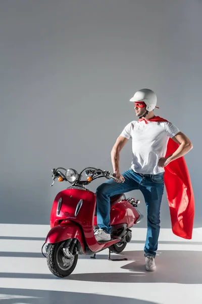 Man in protective helmet and superhero costume standing at red scooter — Stock Photo