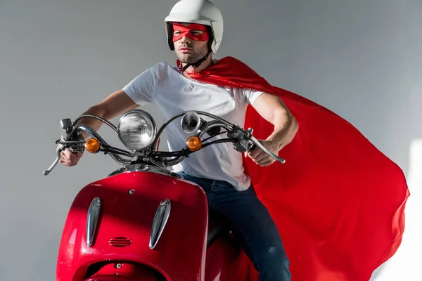 Man in protective helmet and superhero costume riding red scooter — Stock Photo