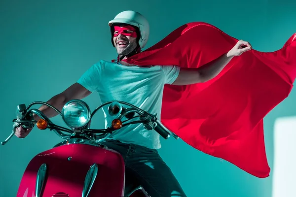 Portrait of happy man in protective helmet and superhero costume riding red scooter — Stock Photo