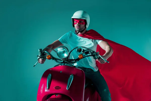 Retrato de homem em capacete protetor, máscara de super-herói e capa montando scooter vermelho — Fotografia de Stock