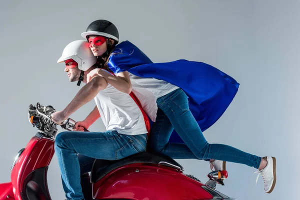 Side view of couple in superhero costumes riding red scooter together — Stock Photo