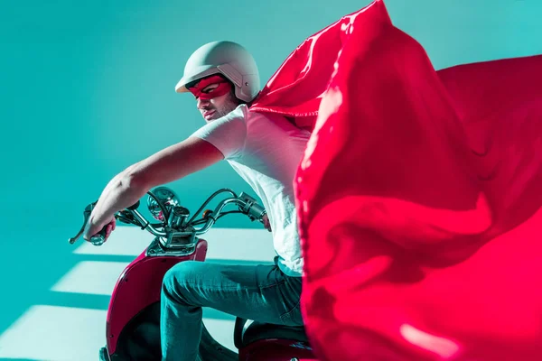 Side view of man in protective helmet and superhero costume on red scooter — Stock Photo