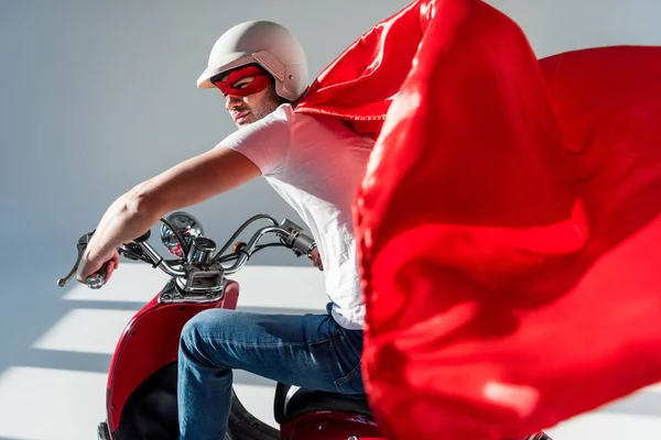 Side view of man in protective helmet and superhero costume on red scooter — Stock Photo
