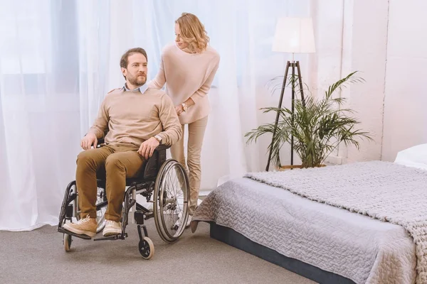 Marido en silla de ruedas y esposa en dormitorio ligero - foto de stock